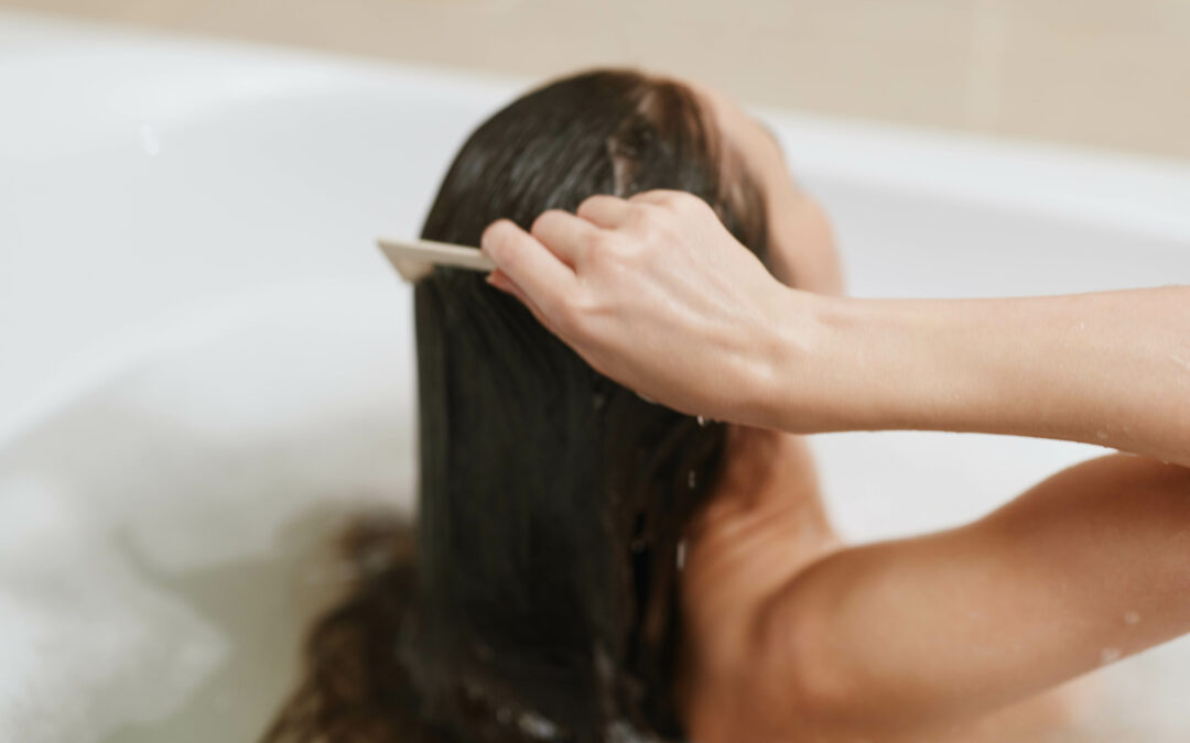 Calm woman combing her wet hair while relaxing in a bathtub, enjoying self care moments. Wellness and beauty routine concept.